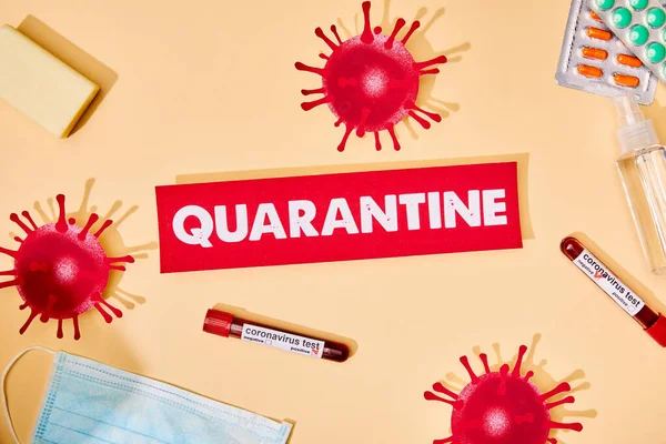 Top view of paper with quarantine lettering near drawn virus, test tubes, soap bar, medical mask, pills and hand sanitizer on beige — Stock Photo