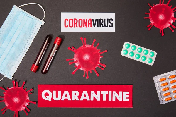 Top view of papers with coronavirus and quarantine lettering near drawn virus, test tubes, medical mask, and pills on black — Stock Photo