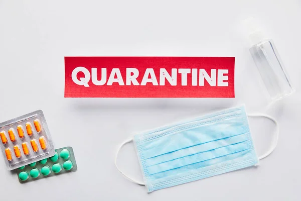 Top view of paper with quarantine lettering near medical mask, pills and hand sanitizer on white — Stock Photo