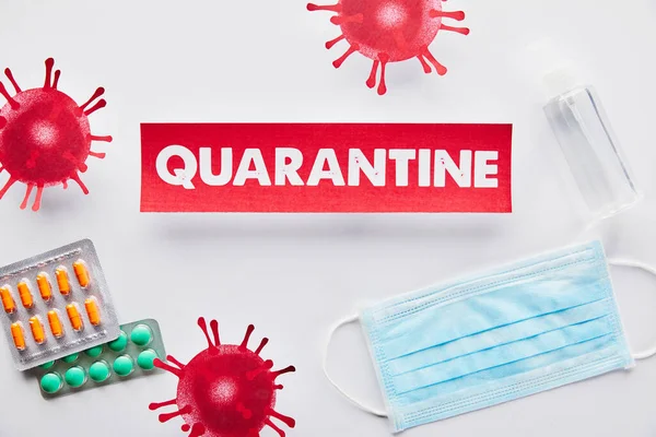 Top view of paper with quarantine lettering near drawn virus, medical mask, pills and hand sanitizer on white — Stock Photo