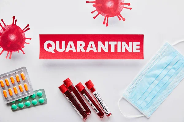 Top view of paper with quarantine lettering near drawn virus, test tubes with coronavirus test, medical mask and pills on white — Stock Photo