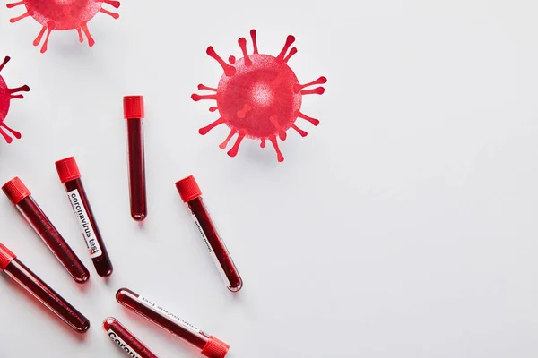 Top view of test tubes with blood samples and coronavirus test lettering near drawn virus on white — Stock Photo