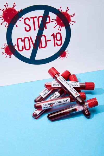 Placard with stop covid-19 lettering near test tubes with samples of blood and coronavirus test lettering on blue — Stock Photo