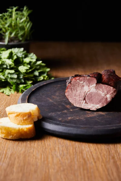 Foco seletivo de presunto saboroso a bordo perto de salsa e baguete em mesa de madeira isolada em preto — Stock Photo