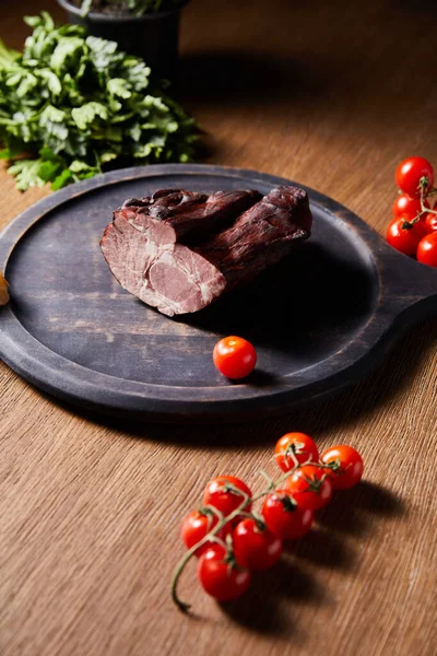 Foco seletivo de presunto saboroso a bordo perto de salsa, tomates cereja na mesa de madeira — Stock Photo