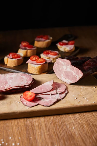 Selective focus of tasty ham slices, cherry tomatoes on cutting board near canape — Stock Photo