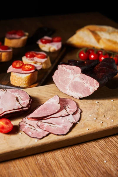 Selective focus of tasty ham slices, cherry tomatoes on cutting board near canape — Stock Photo