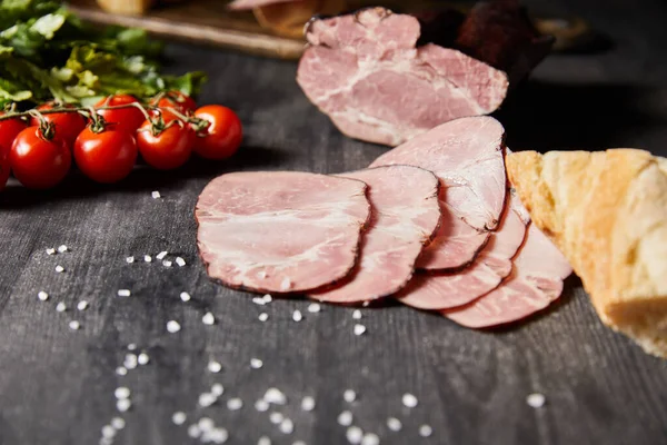 Selective focus of tasty ham sliced ham, cherry tomatoes, parsley, salt and baguette on wooden grey table — Stock Photo