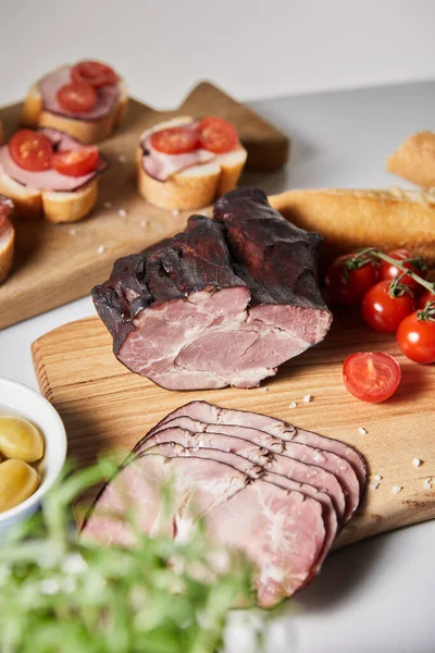 Selective focus of tasty ham on cutting board with cherry tomatoes, olives and baguette near canape — Stock Photo