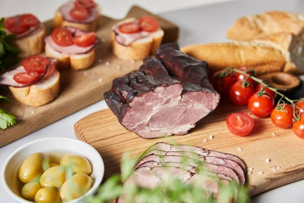 Selective focus of tasty ham on cutting board with cherry tomatoes, olives and baguette near canape — Stock Photo