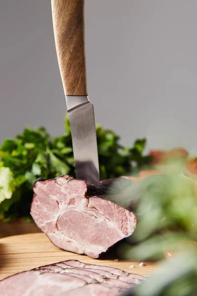 Selective focus of knife in tasty ham on cutting board with parsley isolated on grey — Stock Photo