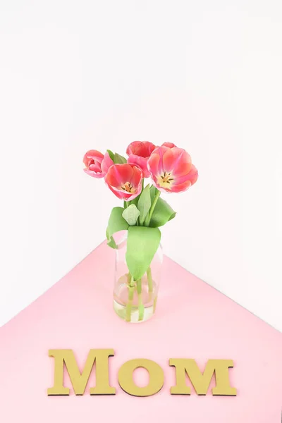 Spring tulips in vase near mom lettering on pink and white background — Stock Photo