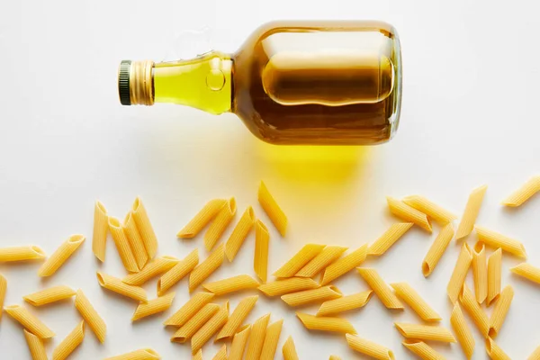 Vista dall'alto della bottiglia di olio d'oliva vicino alla pasta su sfondo bianco — Foto stock