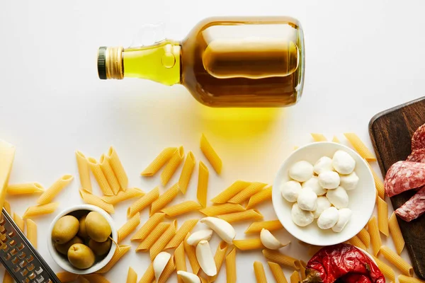 Верхний вид бутылки оливкового масла и макарон с ингредиентами на белом фоне — стоковое фото
