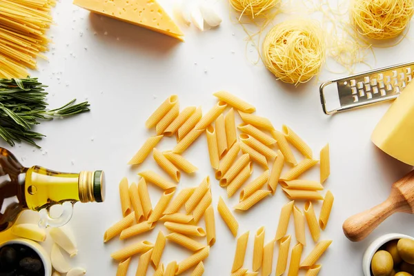 Top view of pasta, rolling pin, grater, bottle of olive oil and ingredients on white — Stock Photo