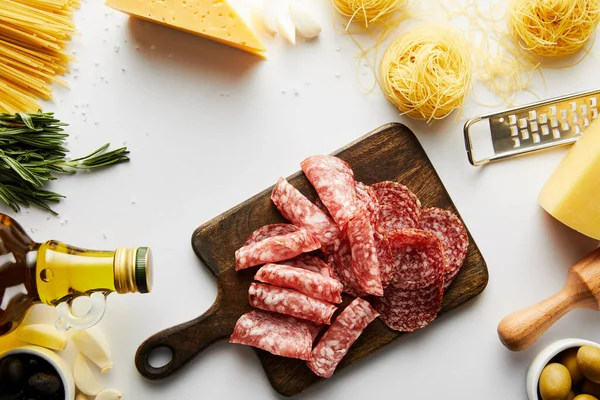 Vista superior de bandeja de carne, pasta, botella de aceite de oliva, rodillo, rallador e ingredientes sobre fondo blanco - foto de stock