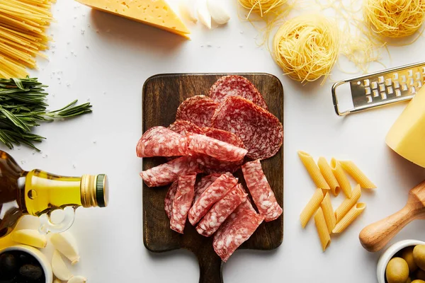 Vista superior de bandeja de carne, pasta, botella de aceite de oliva, rallador e ingredientes sobre fondo blanco - foto de stock
