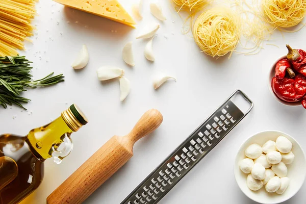 Vista superior do rolo de rolo, garrafa de azeite, ralador, massas e ingredientes em branco — Fotografia de Stock