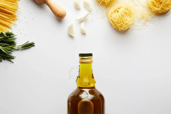 Vista superior de la botella de aceite de oliva, rodillo, pasta, ajo y romero sobre fondo blanco - foto de stock