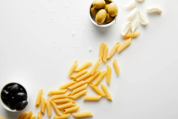 Top view of pasta, sea salt, garlic and bowls with olives on white background — Stock Photo