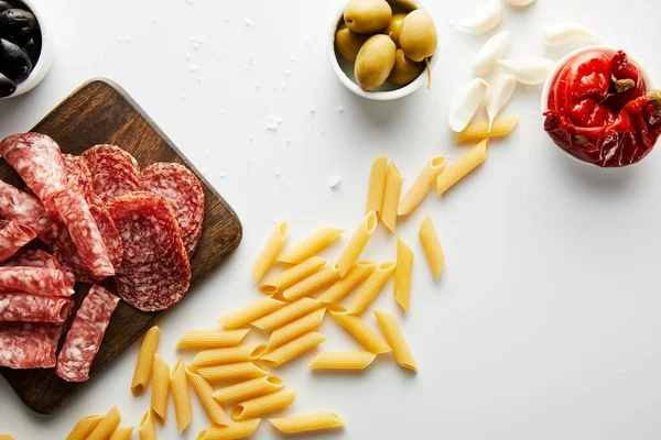 Vista dall'alto pasta, sale marino, aglio, piatto di carne e ciotole con olive e peperoncino marinato su fondo bianco — Foto stock