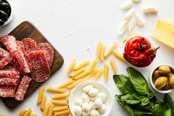 Vista superior de pasta, bandeja de carne, hojas de albahaca e ingredientes sobre fondo blanco - foto de stock