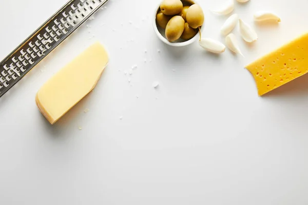 Top view of grater, cheese, garlic and bowl with olives on white background — Stock Photo