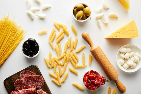 Vista dall'alto di piatto di carne, mattarello, pasta e ingredienti su sfondo bianco — Foto stock