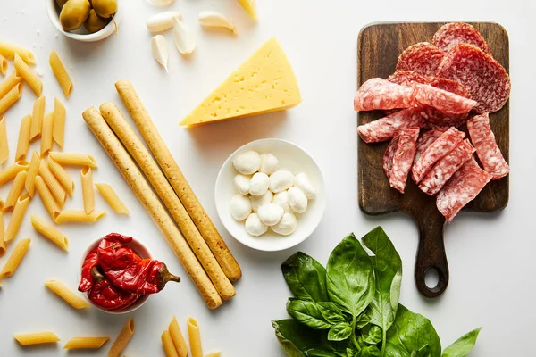 Vista dall'alto di piatti di carne, grissini, pasta e ingredienti su sfondo bianco — Foto stock