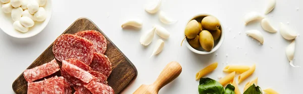 Orientação panorâmica de prato de carne, rolo, macarrão, alho e tigelas com azeitonas e mussarela sobre fundo branco — Fotografia de Stock
