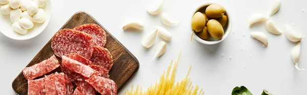 Cultivo panorámico de plato de carne, ajo y cuencos con aceitunas y mozzarella sobre fondo blanco - foto de stock