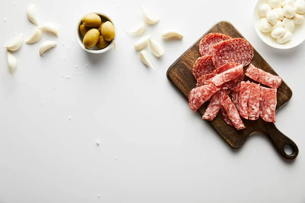 Vista dall'alto di piatto di carne, aglio, sale marino e ciotole con olive e mozzarella su sfondo bianco — Foto stock