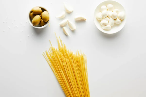 Vue de dessus des spaghettis, ail, sel de mer et bols avec olives et mozzarella sur fond blanc — Photo de stock