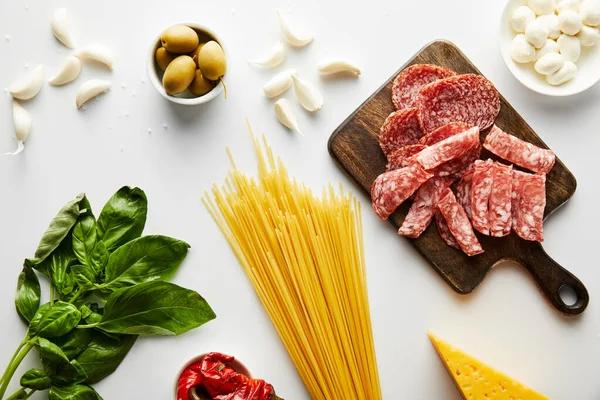 Vista superior de espaguetis, bandeja de carne, hojas de albahaca e ingredientes sobre fondo blanco - foto de stock