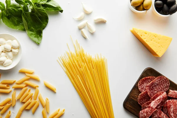 Vista dall'alto di spaghetti, piatto di carne, foglie di basilico e ingredienti su bianco — Foto stock