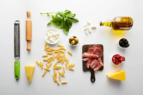 Poser à plat avec plateau de viande, bouteille d'huile d'olive, rouleau à pâtisserie, râpe et ingrédients sur fond blanc — Photo de stock