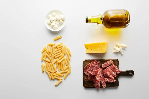 Colocação plana com prato de carne, garrafa de azeite, alho, queijo, macarrão e tigela com mussarela em branco — Fotografia de Stock