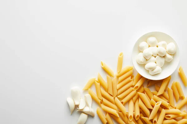 Vista dall'alto di aglio, pasta e ciotola con mozzarella su fondo bianco — Foto stock