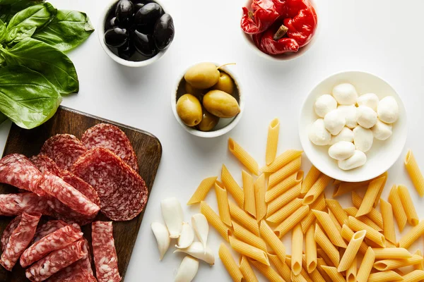 Vista dall'alto di piatto di carne, pasta, foglie di basilico e ingredienti su sfondo bianco — Foto stock