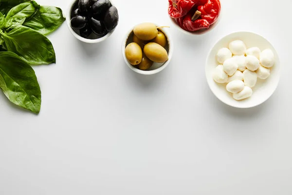 Vista superior de hojas de albahaca y cuencos con ingredientes en blanco - foto de stock