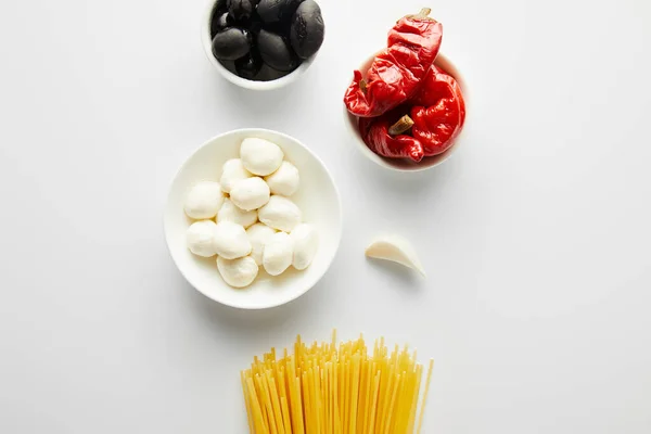 Vista dall'alto di spaghetti, aglio e ciotole con ingredienti su sfondo bianco — Foto stock