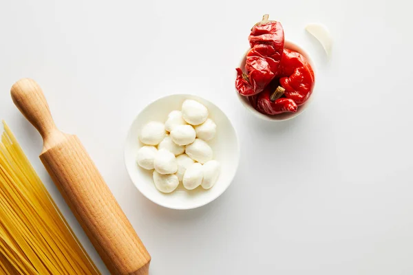 Vista superior de espaguetis, rodillo, ajo y cuencos con ingredientes en blanco - foto de stock