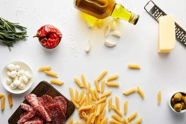 Top view of bottle of olive oil, meat platter, grater, pasta and ingredients on white background — Stock Photo