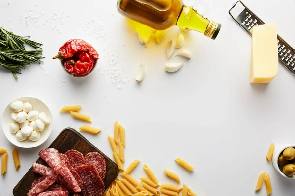 Vista superior da garrafa de azeite, prato de carne, ralador, macarrão e ingredientes em branco — Fotografia de Stock