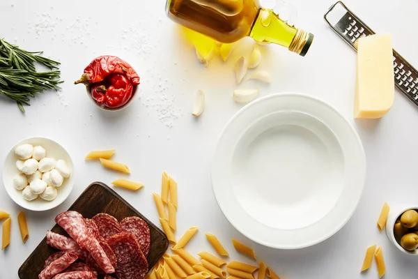 Vista superior do prato, garrafa de azeite, prato de carne, ralador, macarrão e ingredientes em branco — Fotografia de Stock