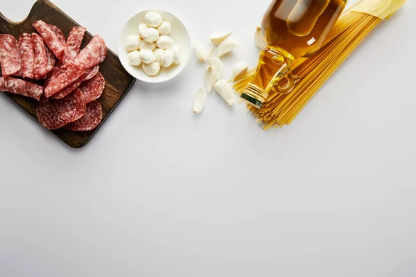 Vista superior de la botella de aceite de oliva, plato de carne, ajo, pasta y tazón con mozzarella en blanco - foto de stock