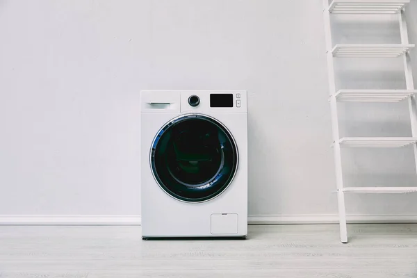 Machine à laver moderne près de rack et mur blanc dans la salle de bain — Photo de stock