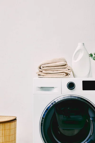 Garrafa de detergente e toalhas na máquina de lavar roupa perto de cesta de lavanderia no banheiro — Fotografia de Stock