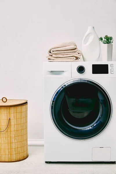 Planta verde, garrafa de detergente e toalhas na máquina de lavar roupa perto de cesta de lavanderia no banheiro — Fotografia de Stock