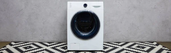 Панорамний знімок сучасної пральної машини біля сірої стіни та декоративного килима у ванній — стокове фото